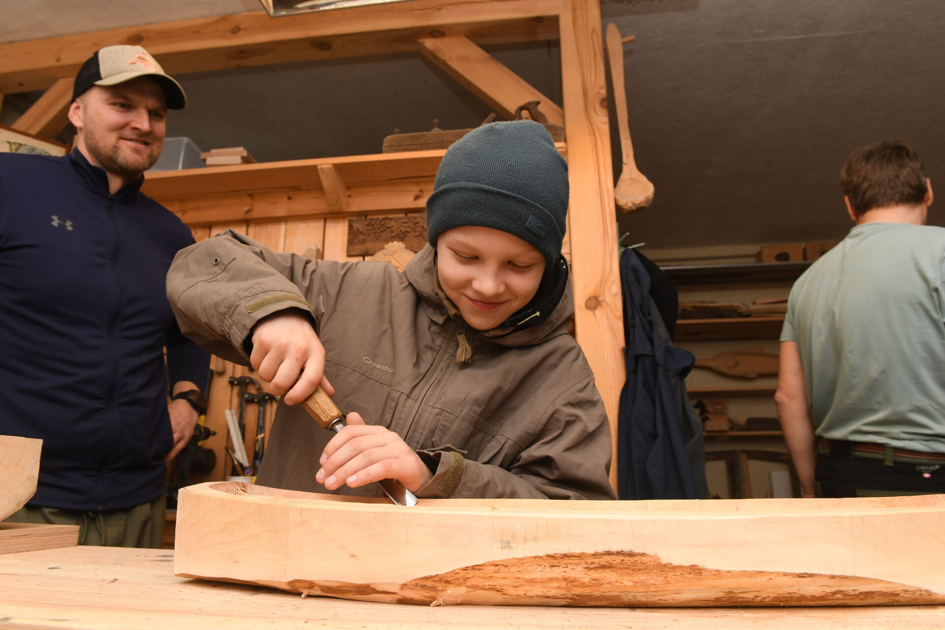 Zēns atrodas galdnieka darbnīcā un grebj koku
